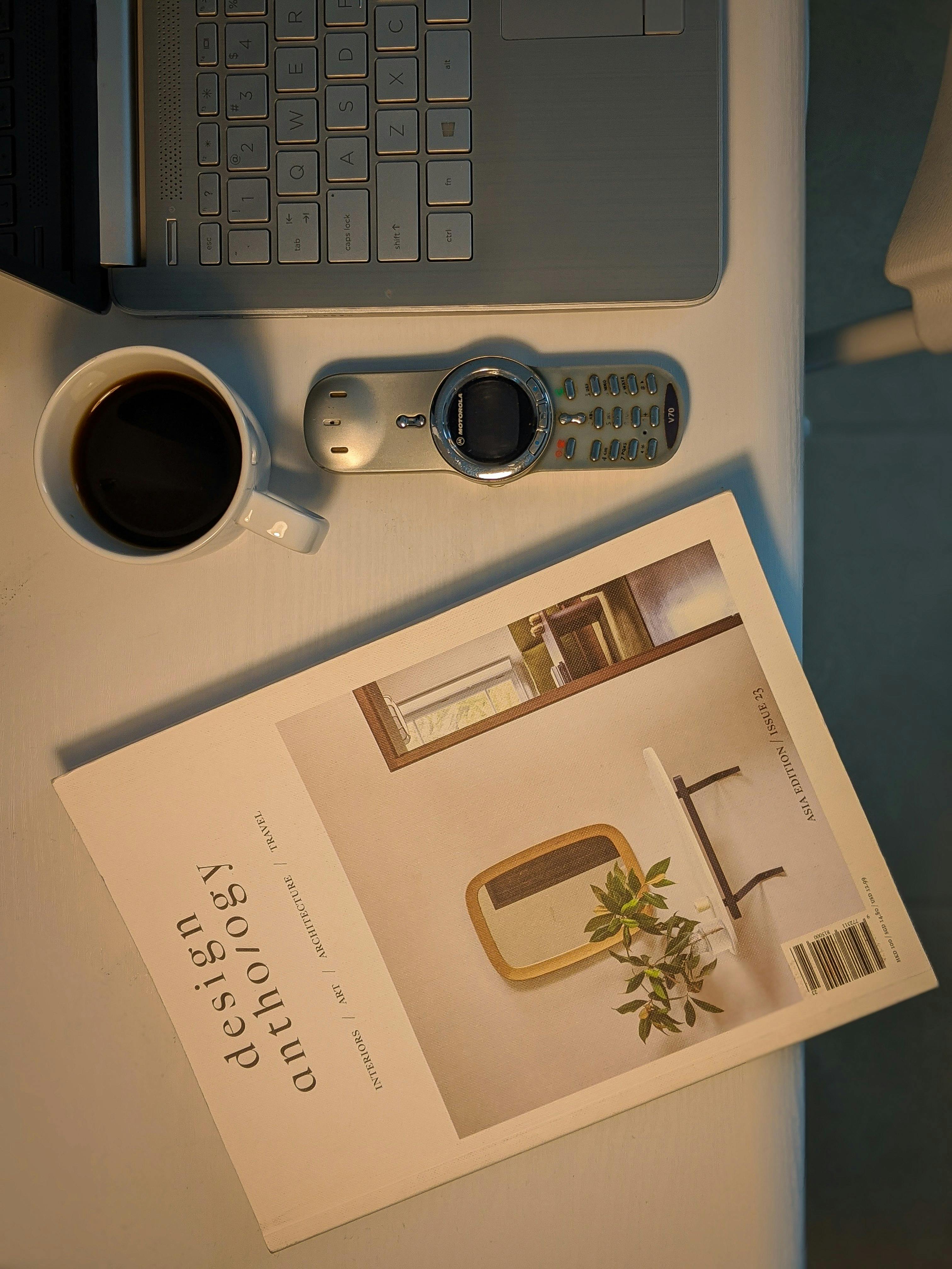 grátis Layout plano de um espaço de trabalho com um laptop, café, controle remoto e revista de design sobre uma mesa. Foto profissional