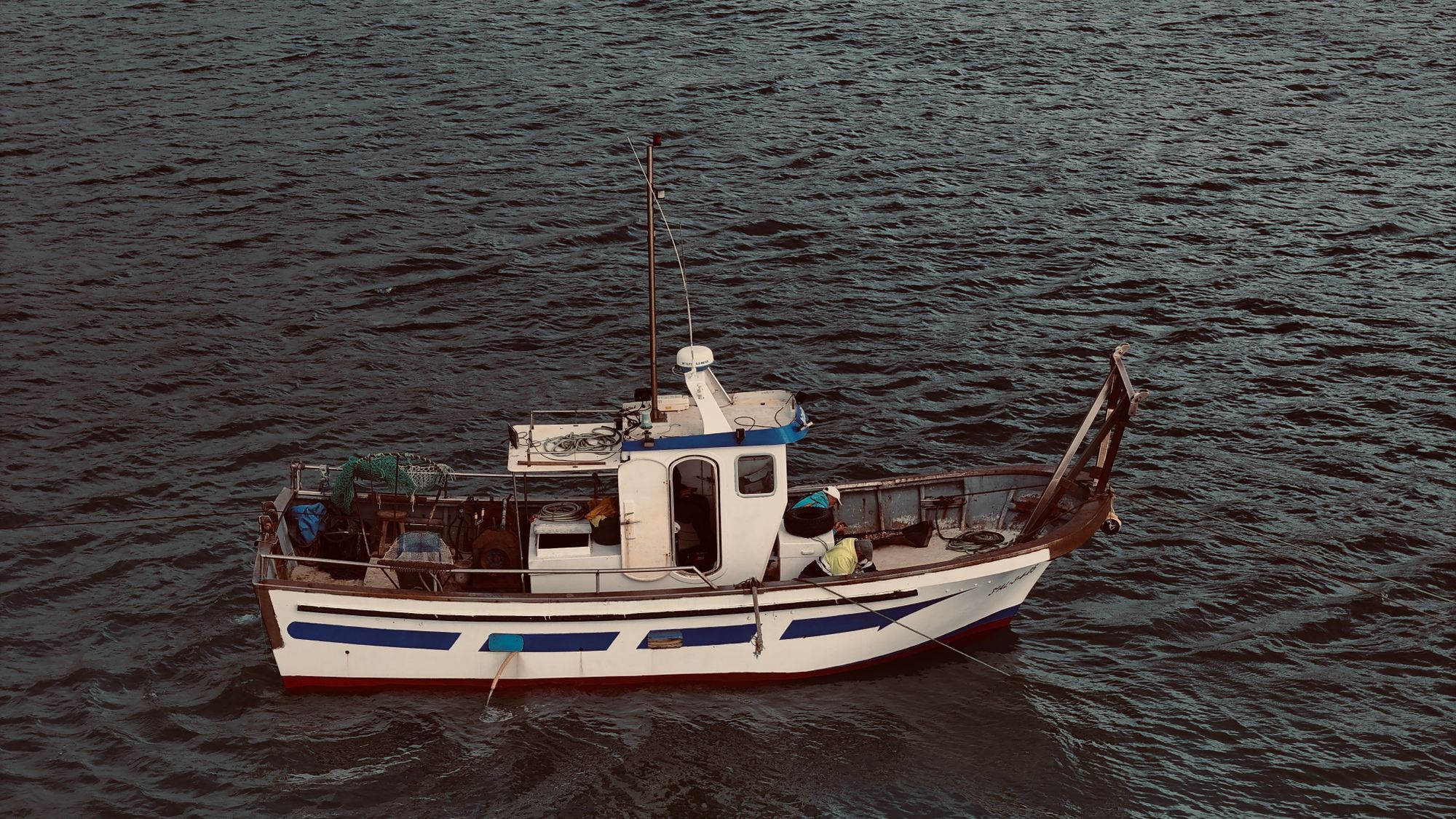 Barco pesquero de casco oscuro navegando en mar abierto bajo un cielo despejado