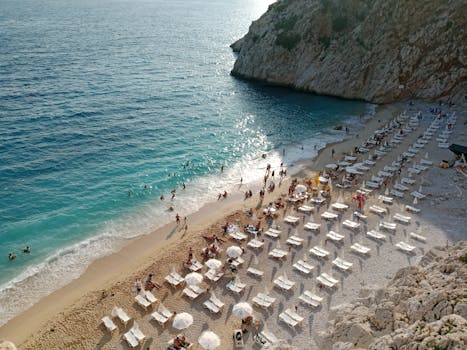 A vibrant beach scene with sunbathers, lounge chairs, and crystal-clear water under the sun.