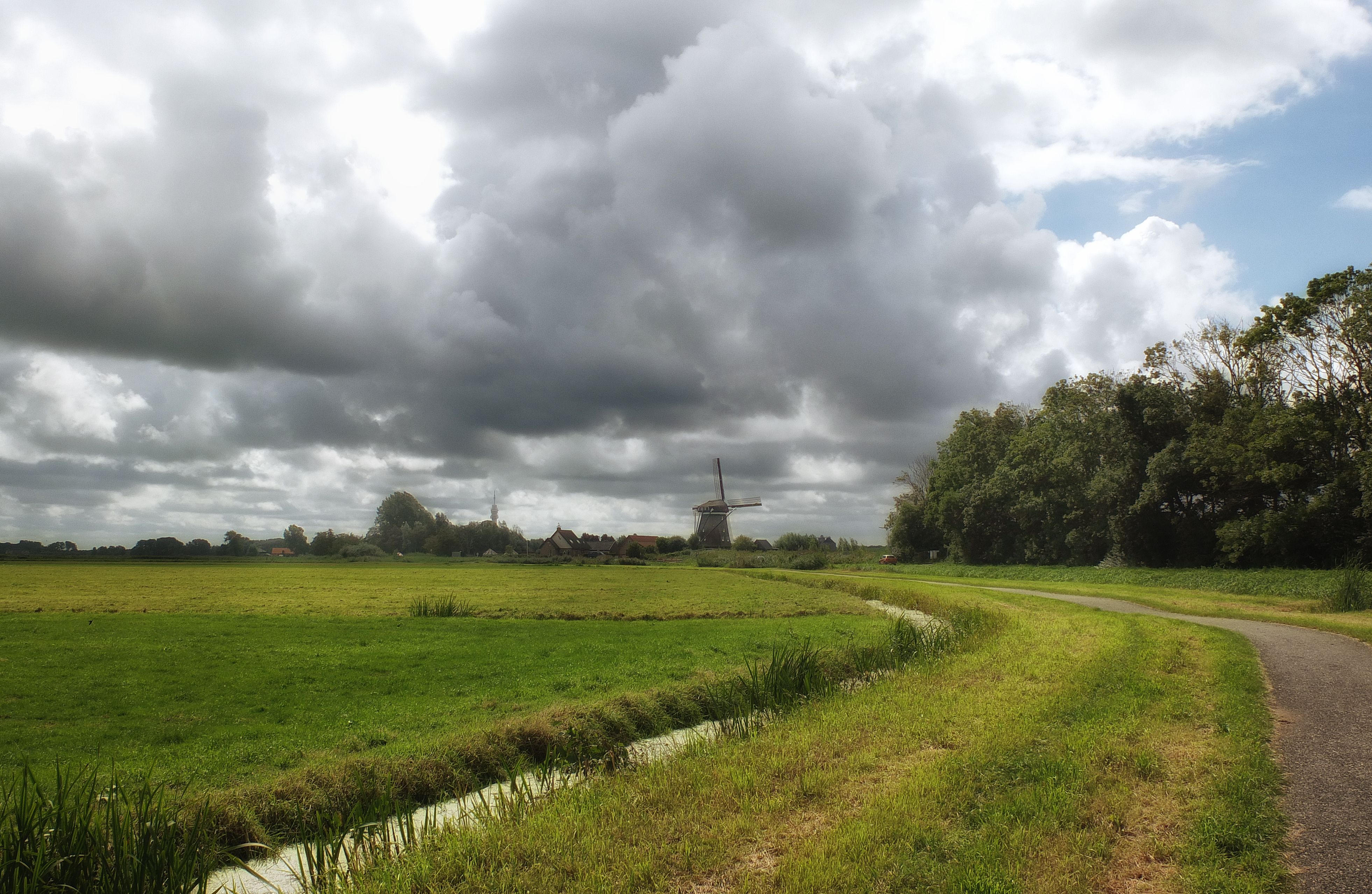 Serene landscape featuring a traditional Dutch windmill and vast green fields under a dramatic sky in Halfweg, Netherlands.