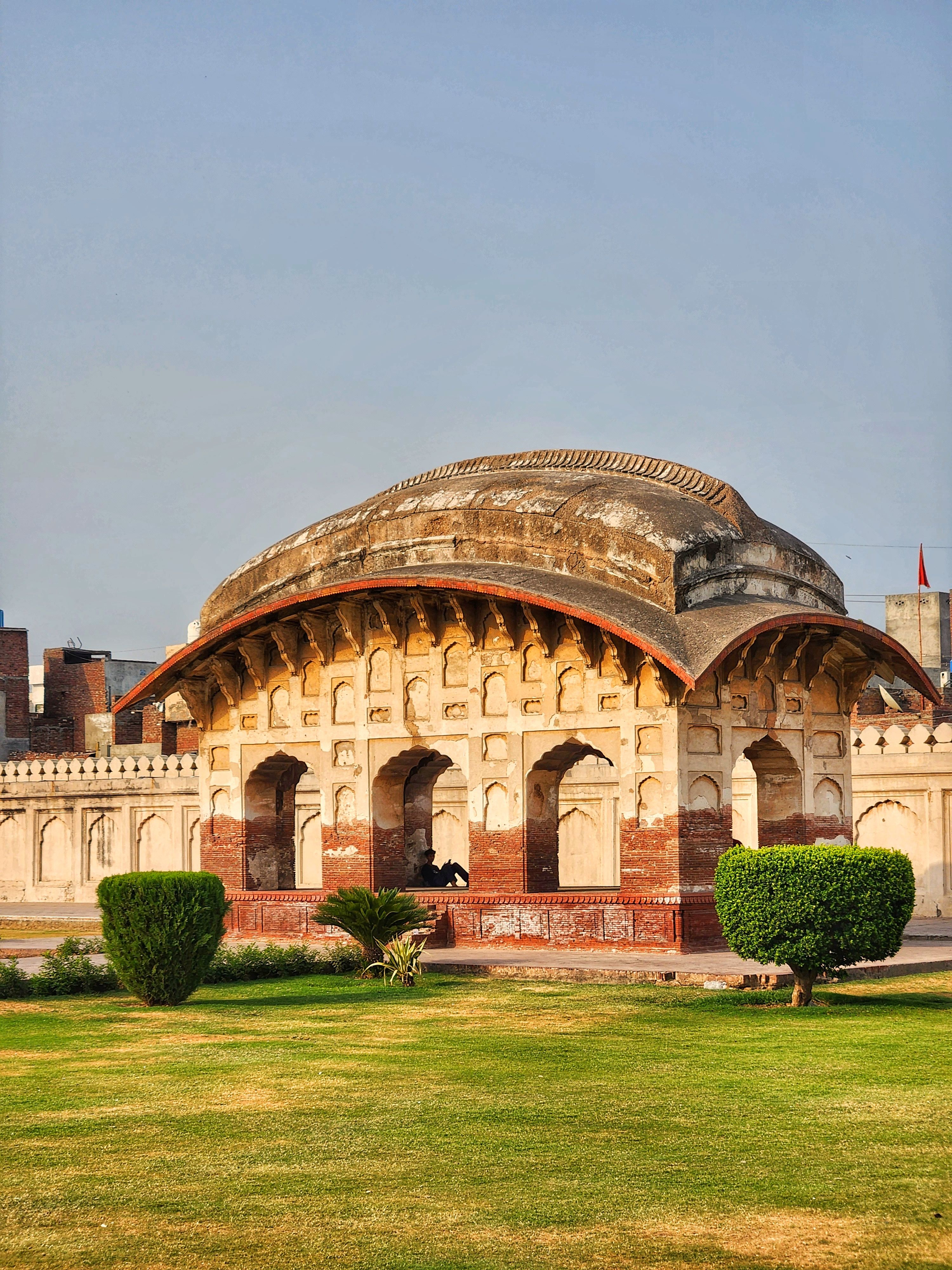 Ancient pavilion with intricate design in a lush garden under clear skies.
