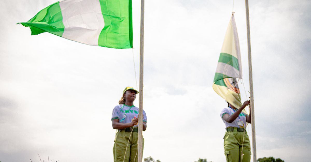 Two youth corps members participate in a flag-raising ceremony outdoors in Kaduna, Nigeria.