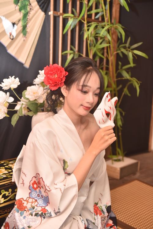 Free A woman wearing a traditional kimono holds a kitsune mask in a beautifully decorated indoor setting. Stock Photo
