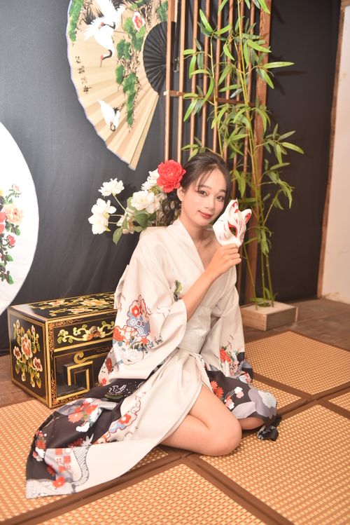 Free Young woman in a kimono holding a traditional mask, showcasing Japanese culture with a floral backdrop. Stock Photo