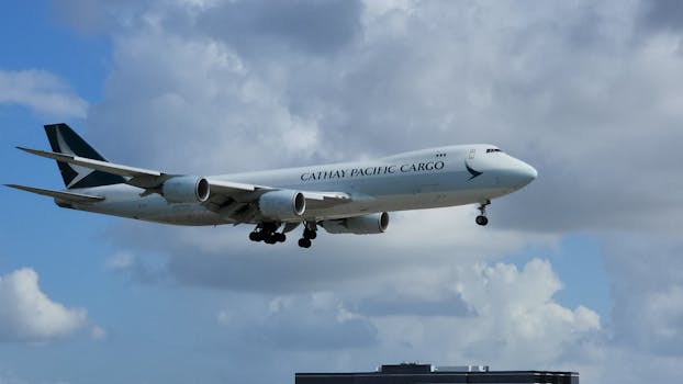 Flying Cathay Pacific cargo plane against a cloudy sky, preparing to land.