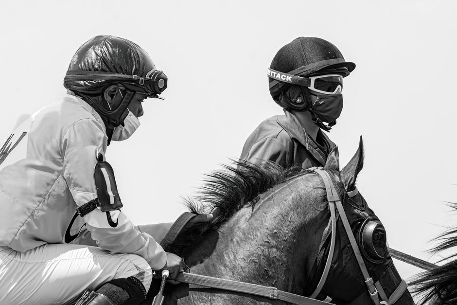 Two jockeys on horses, in black and white, during a race.