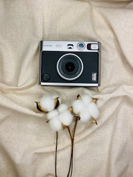 A vintage camera and cotton flowers on beige fabric for a soft, artistic still life photo.