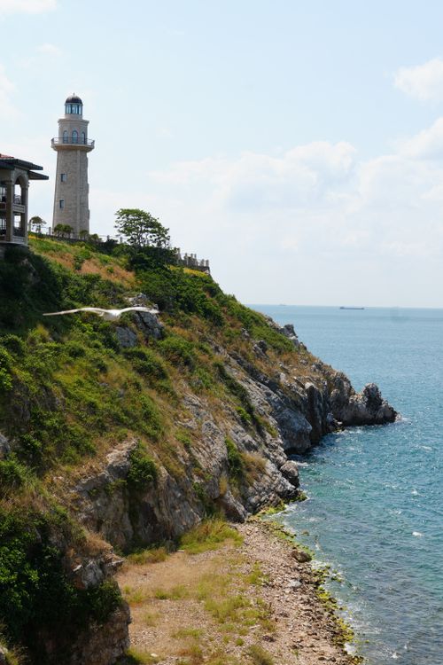 Free Lighthouse perched on a rocky cliff by the ocean on a sunny day. Stock Photo