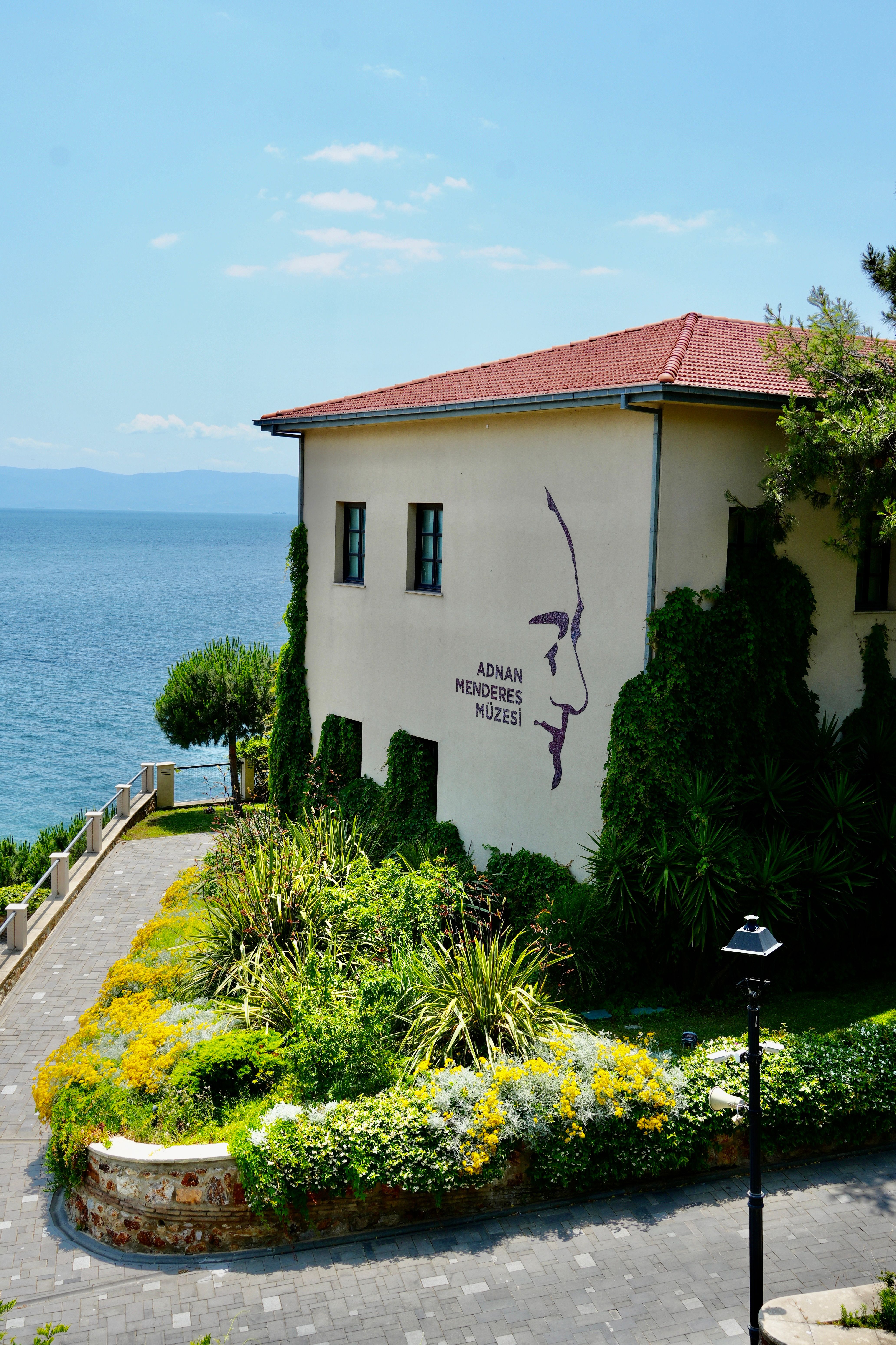 Scenic view of Adnan Menderes Museum by the sea, adorned with lush greenery and summer flowers.