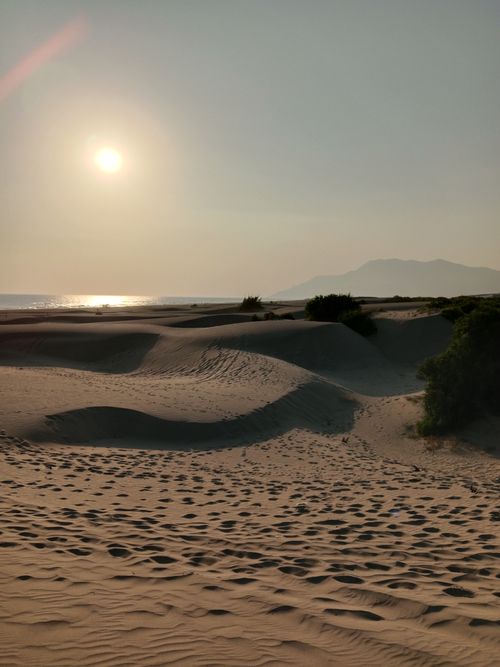 Free Tranquil sunset casting warm light over expansive desert sand dunes with distant mountains. Stock Photo