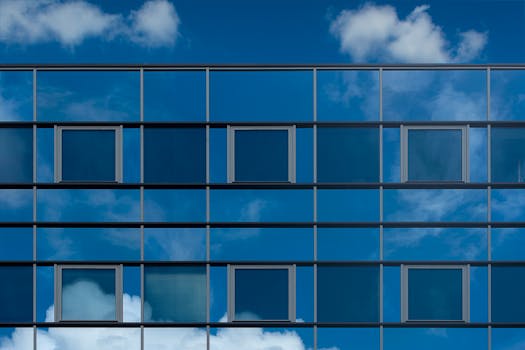Facade of a modern glass building reflecting the blue sky and clouds.