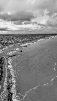 Aerial view of a coastal city with dramatic clouds and ocean waves.