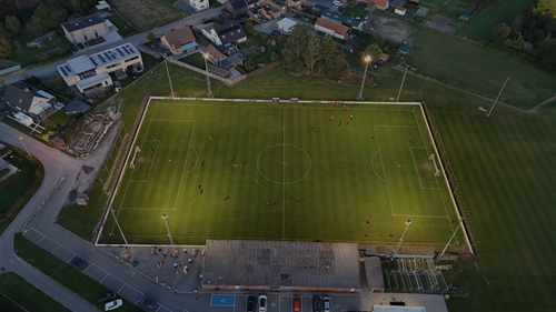 Free Aerial shot of a soccer field at dusk in België with players practicing under floodlights. Stock Photo