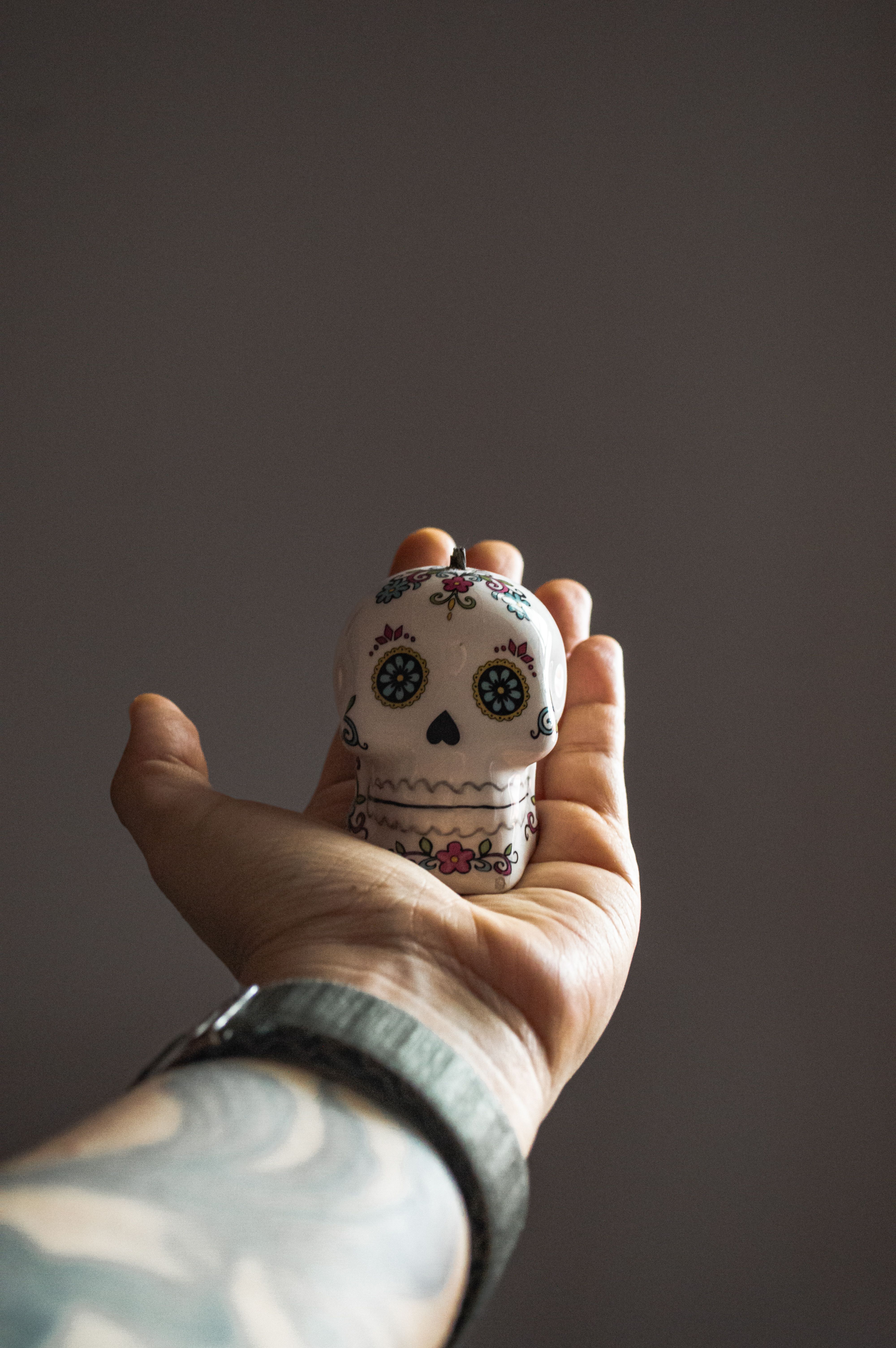 Tattooed hand holding a decorative sugar skull, symbolizing Day of the Dead celebrations.