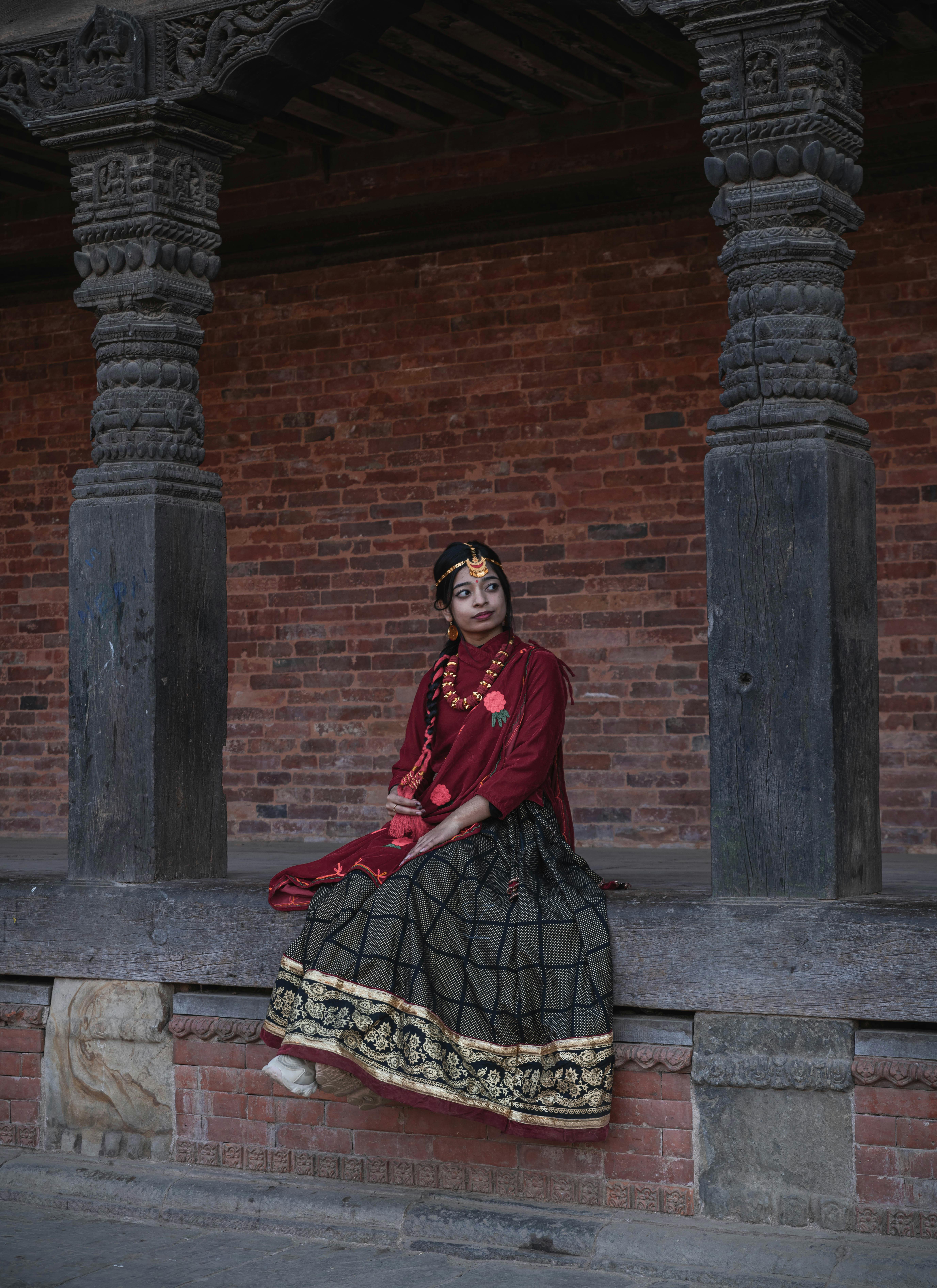A woman in traditional Nepali dress sits by historic architecture in Bhaktapur, Nepal.