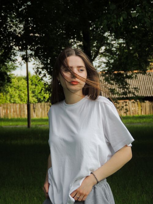 Free A young woman stands in a lush outdoor setting, hair blowing gently in the breeze. Stock Photo