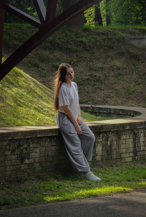 Free A young woman in casual attire relaxes outdoors by a brick wall, capturing a serene, peaceful moment. Stock Photo