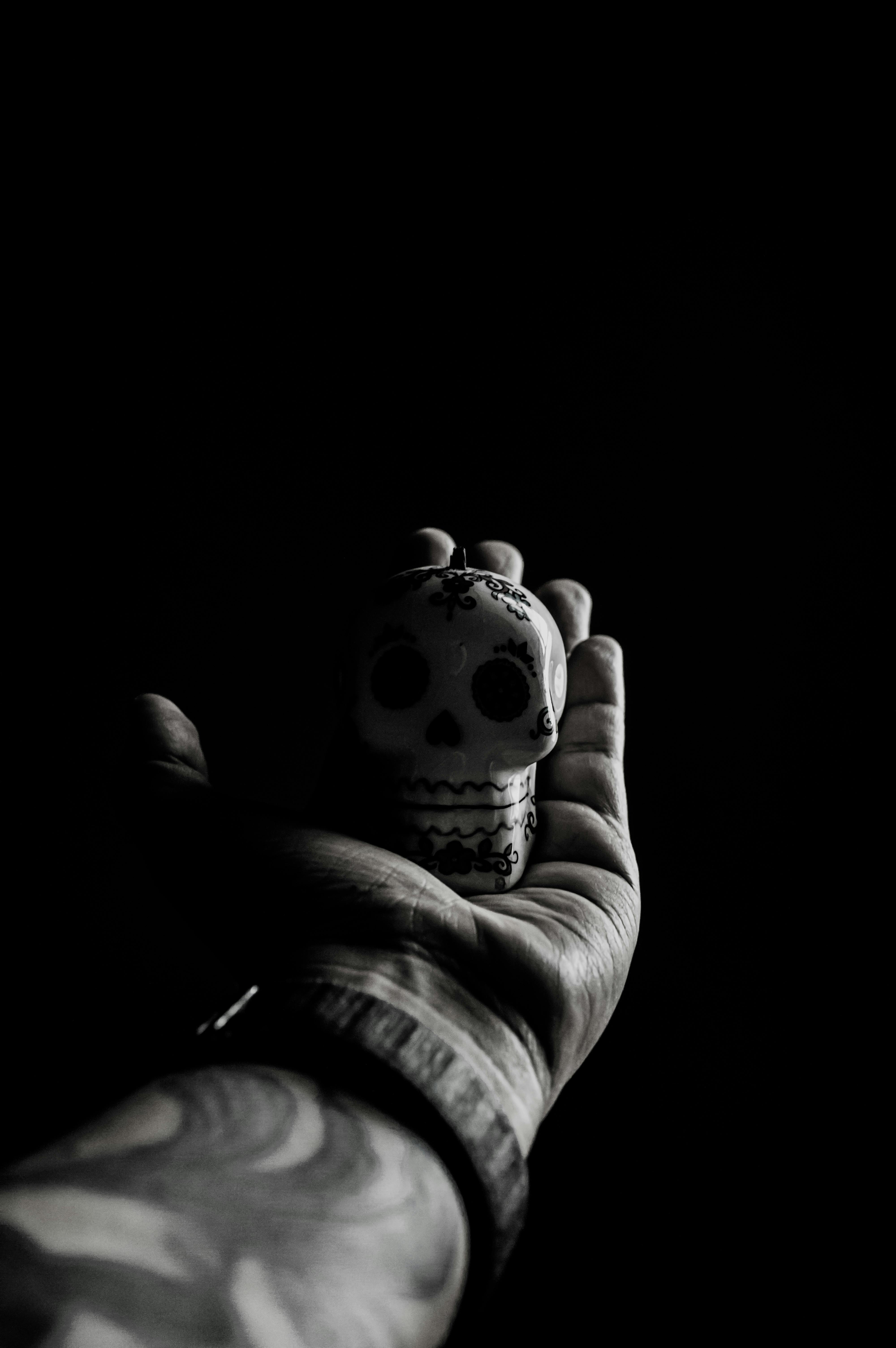 Безкоштовне Татуйована рука, що тримає мініатюрний цукровий череп у драматичній чорно-білій композиції. стокове фото