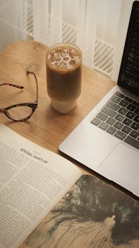A serene workspace with iced coffee, open book, and laptop, perfect for work or study.