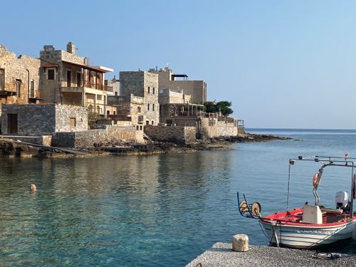 Free Rustic stone buildings by the sea in a serene Greek coastal village with a small fishing boat. Stock Photo