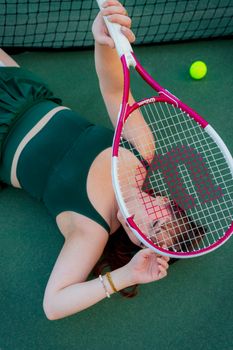 Artistic portrait of a woman in stylish tennis attire lying on the court with a racket.
