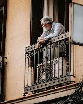Elderly man leaning on a decorative balcony in Madrid, Spain during the day.