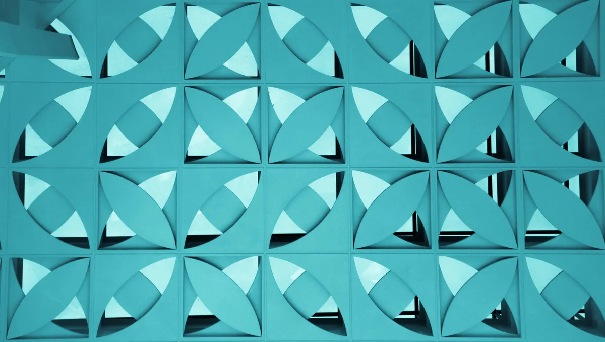 Teal blue geometric pattern wall featuring repeating square modules with intersecting circular petal shapes and white cutouts.