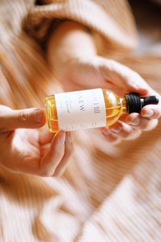 Delicate hand holding a natural skincare serum bottle, showcasing minimalist packaging and gentle lighting.