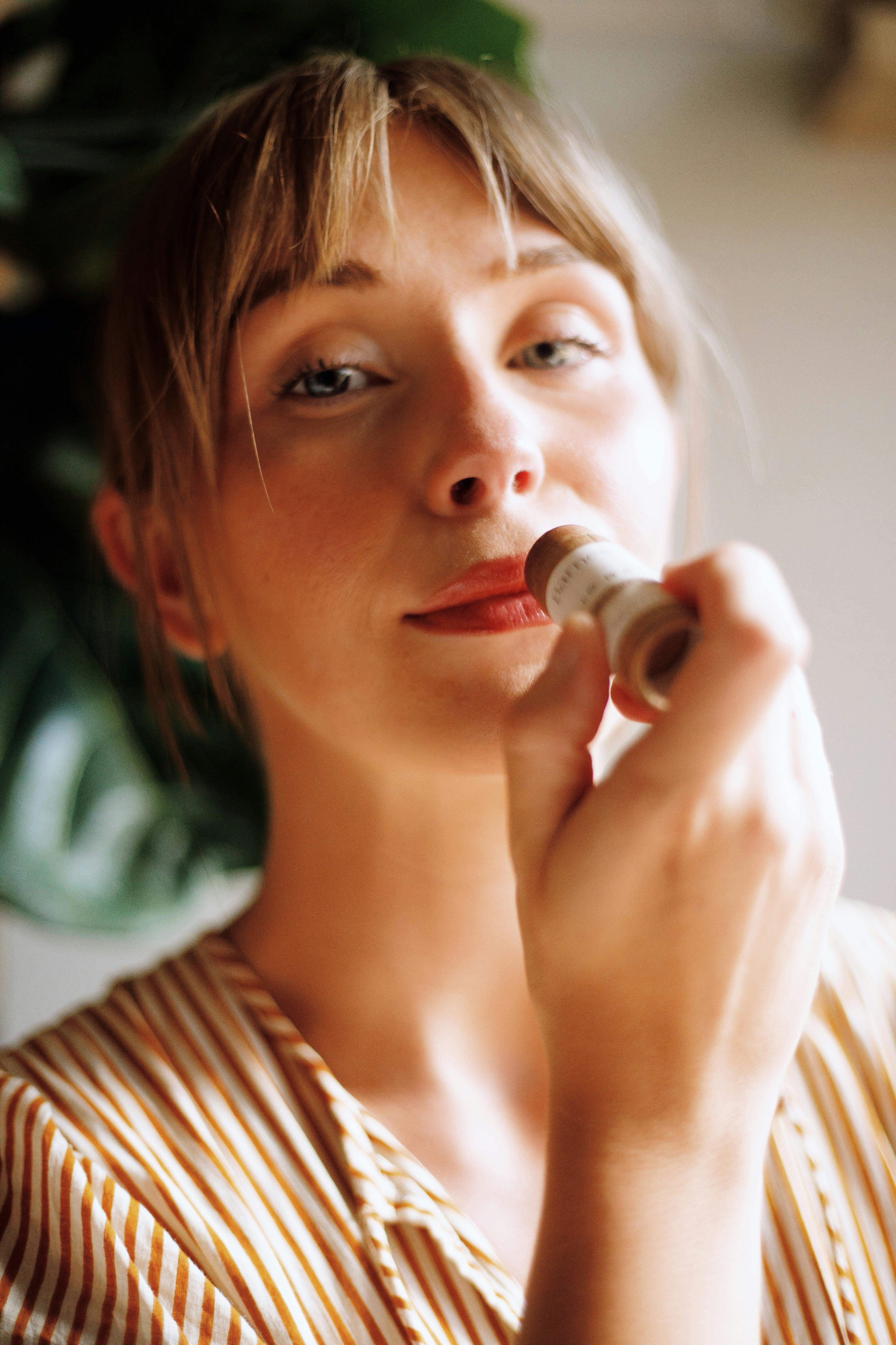 Free A woman applies natural lip balm in soft light, embracing holistic beauty. Stock Photo