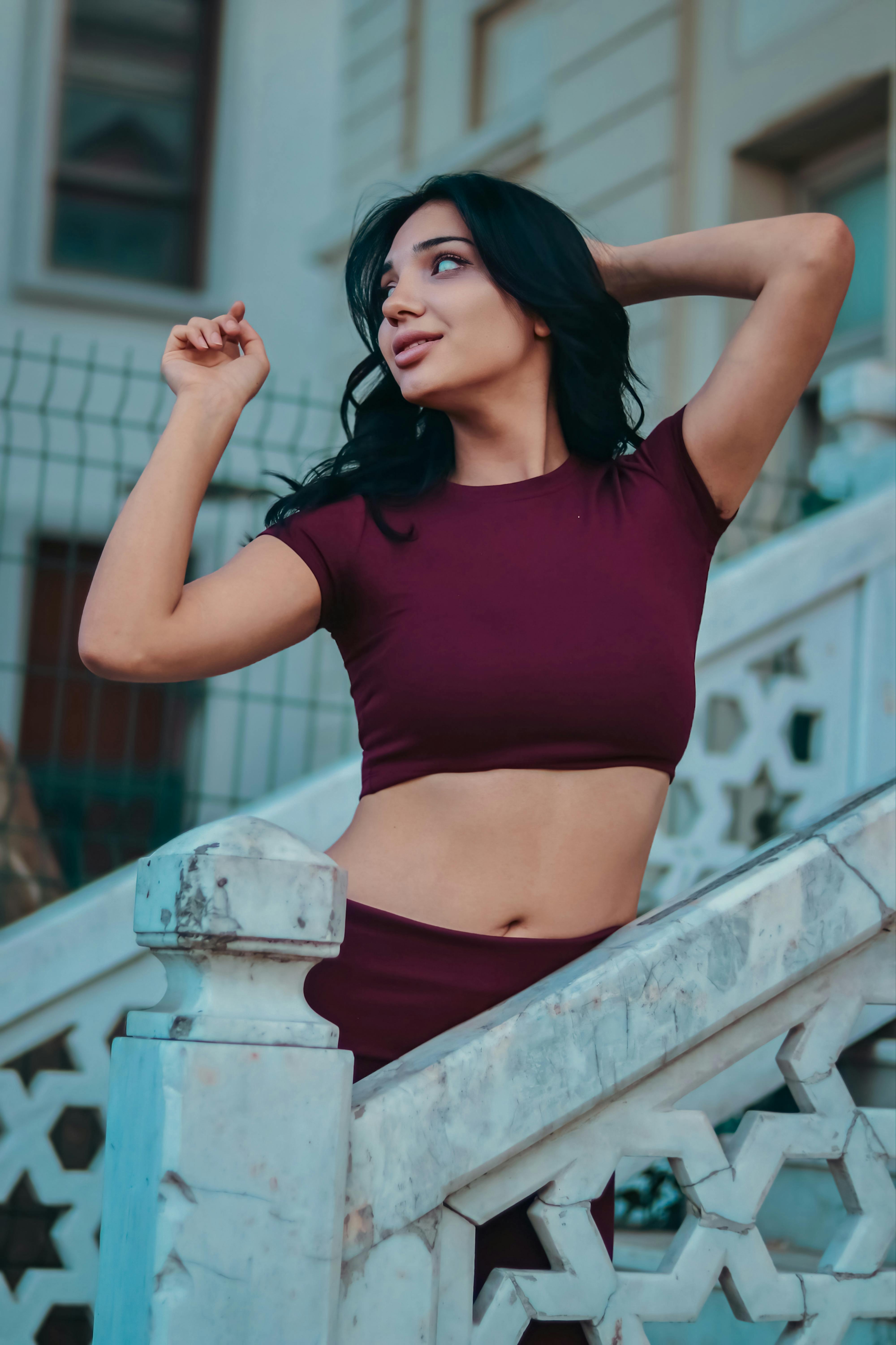 Stylish woman in burgundy outfit poses gracefully on an elegant marble staircase outdoors.