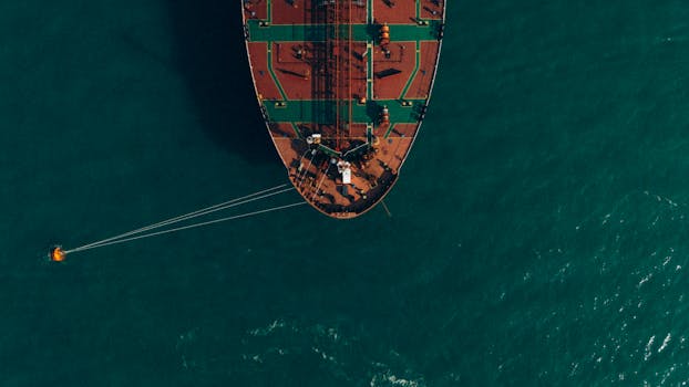 An aerial shot of a cargo ship at sea, showcasing its vibrant deck colors and towing a buoy.