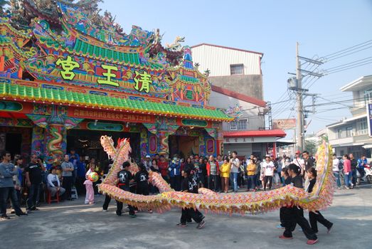 Colorful dragon dance in front of ornate temple during a festive celebration, attracting a diverse crowd.