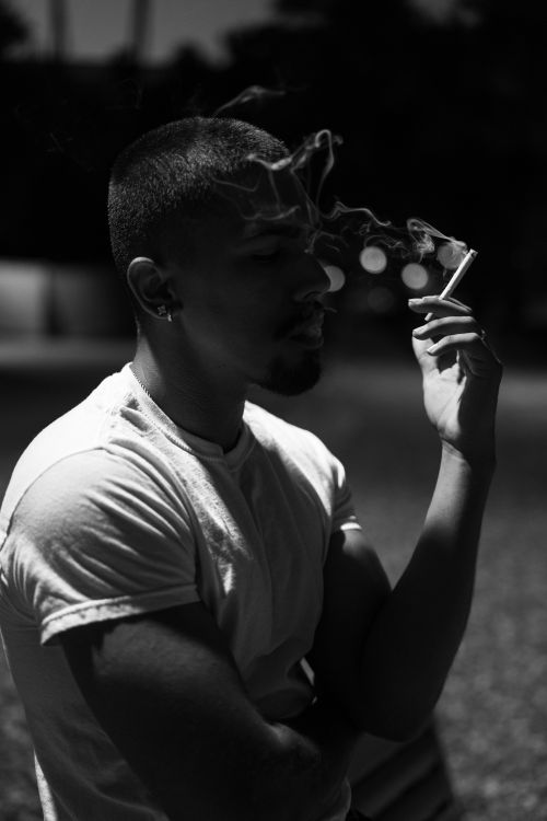 Free Moody black and white portrait of a man smoking in an outdoor setting during nighttime. Stock Photo