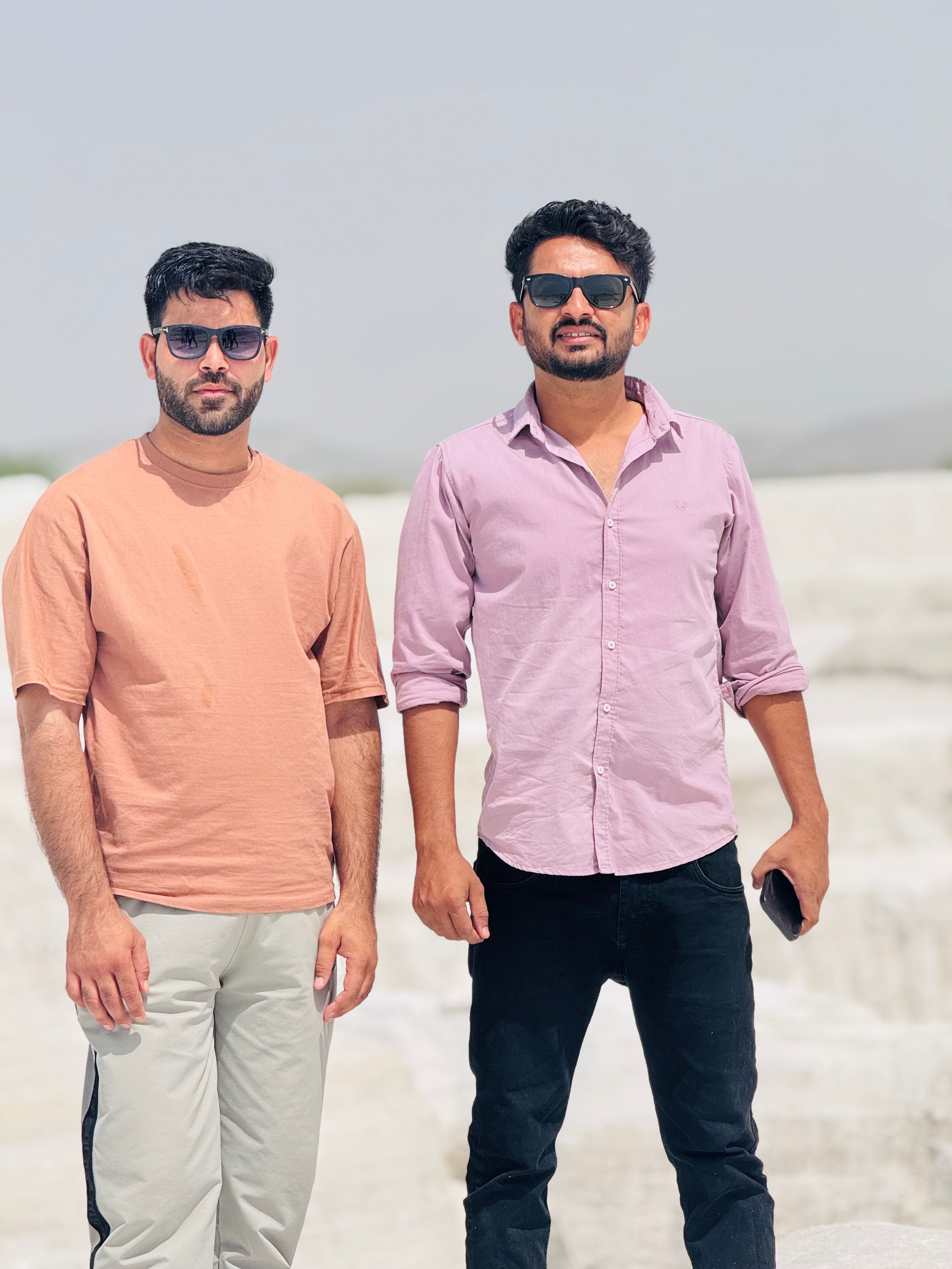 Two men wearing sunglasses in casual shirts standing outdoors on a sunny day.