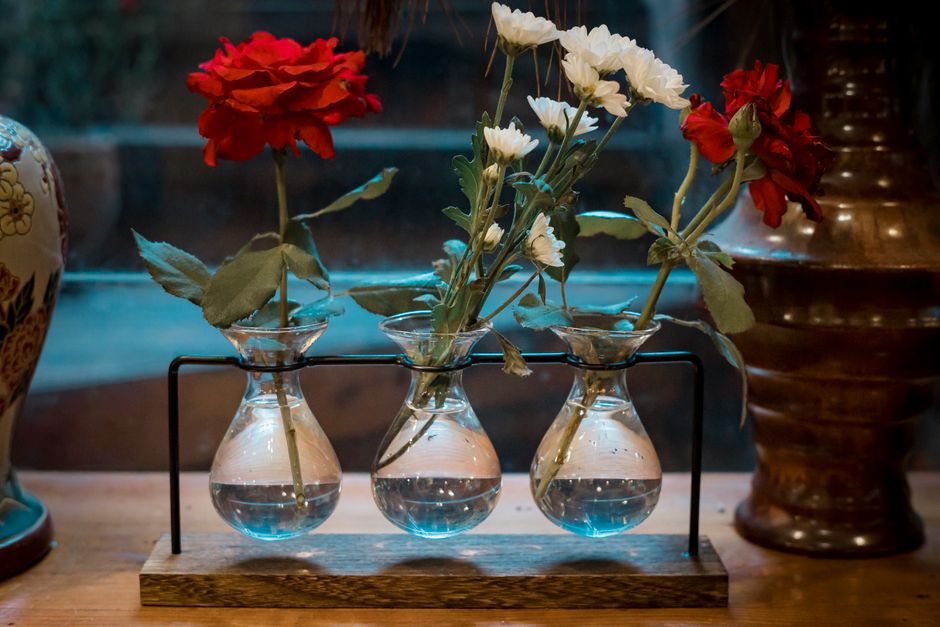Red and white flowers elegantly placed in glass vases on a wooden shelf.