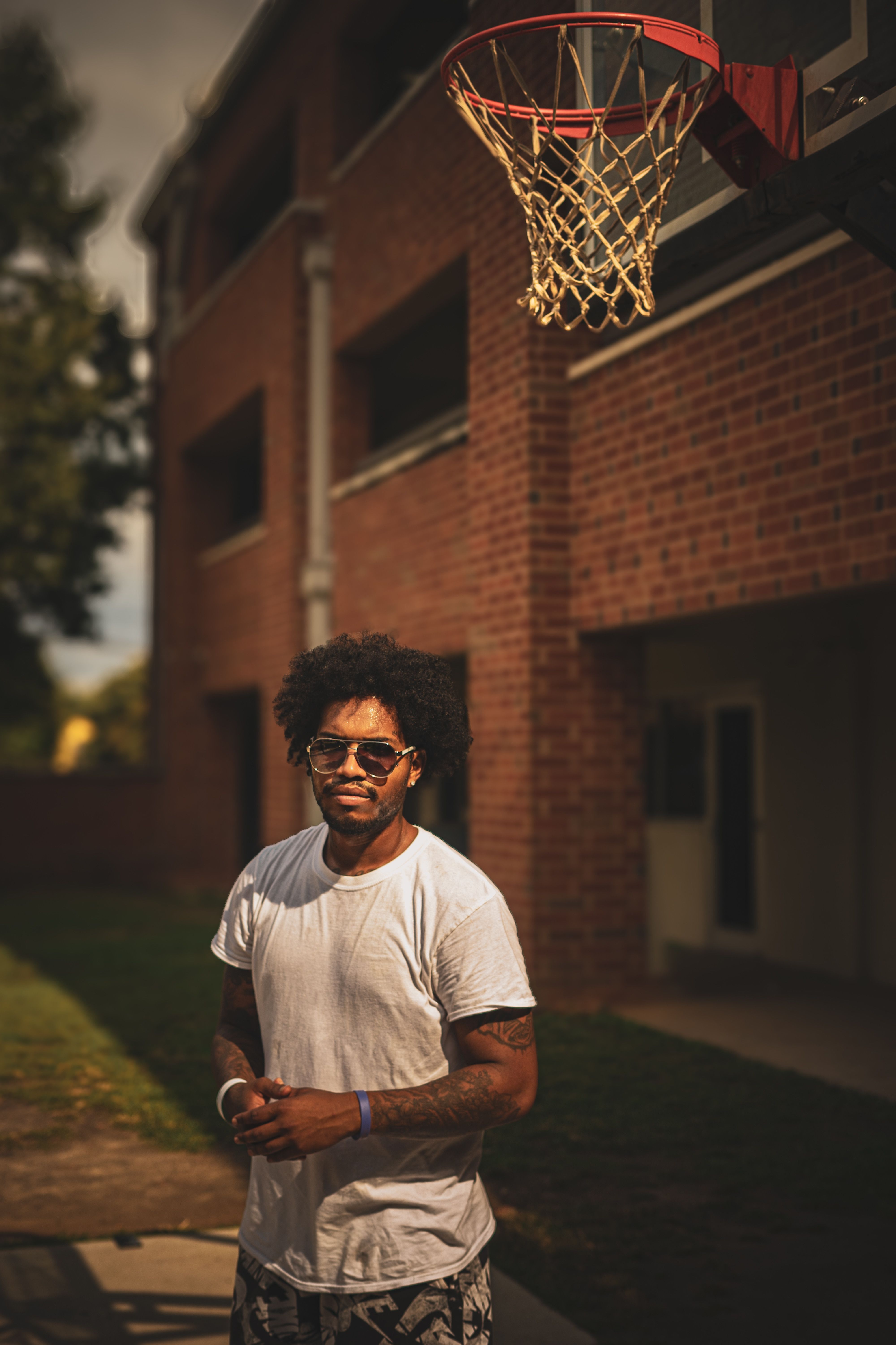 A stylish man in sunglasses poses outdoors by a basketball hoop in Columbia, SC.