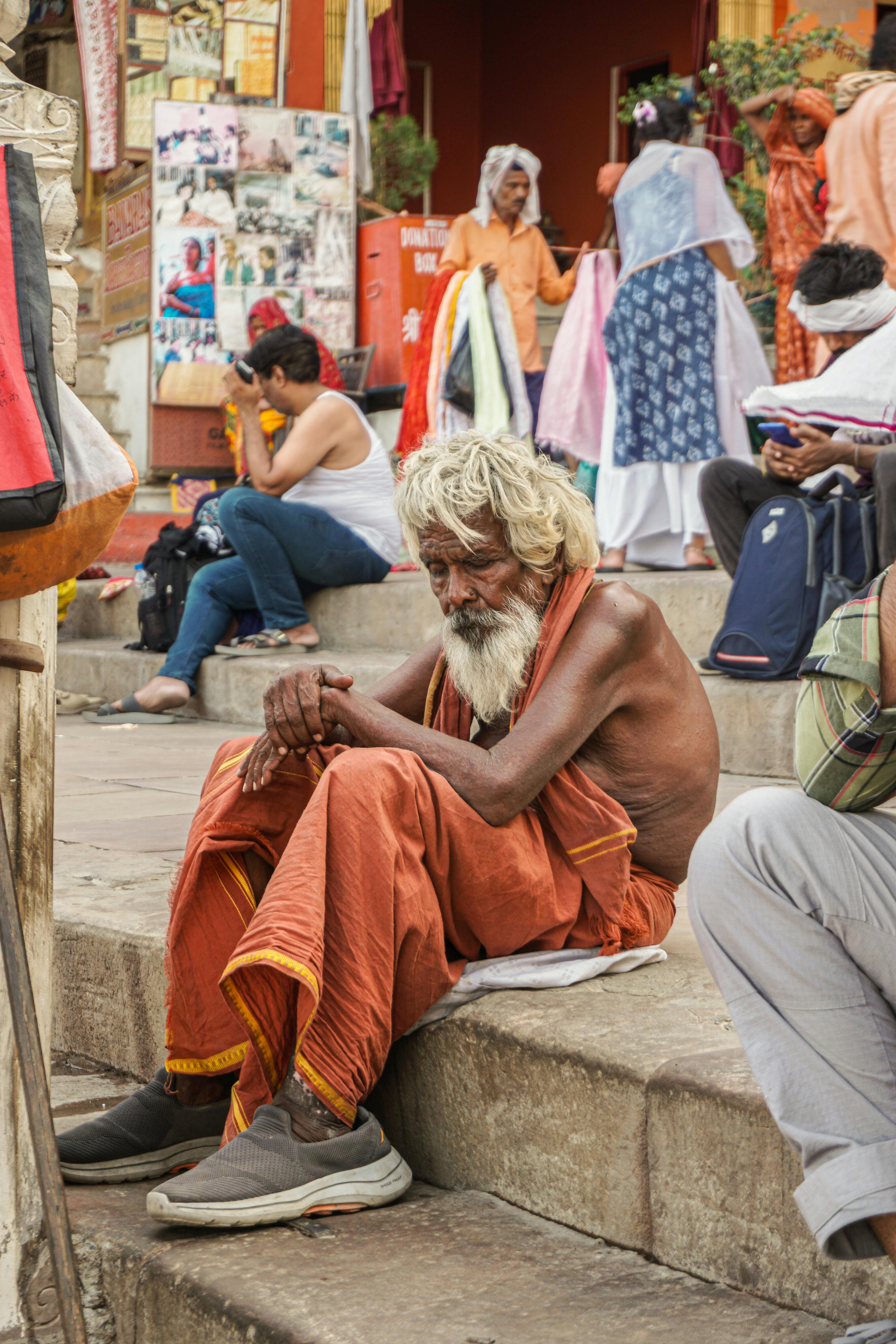 Free A contemplative elderly man sits among vibrant cultural scenes at Varanasi Ghats. Stock Photo