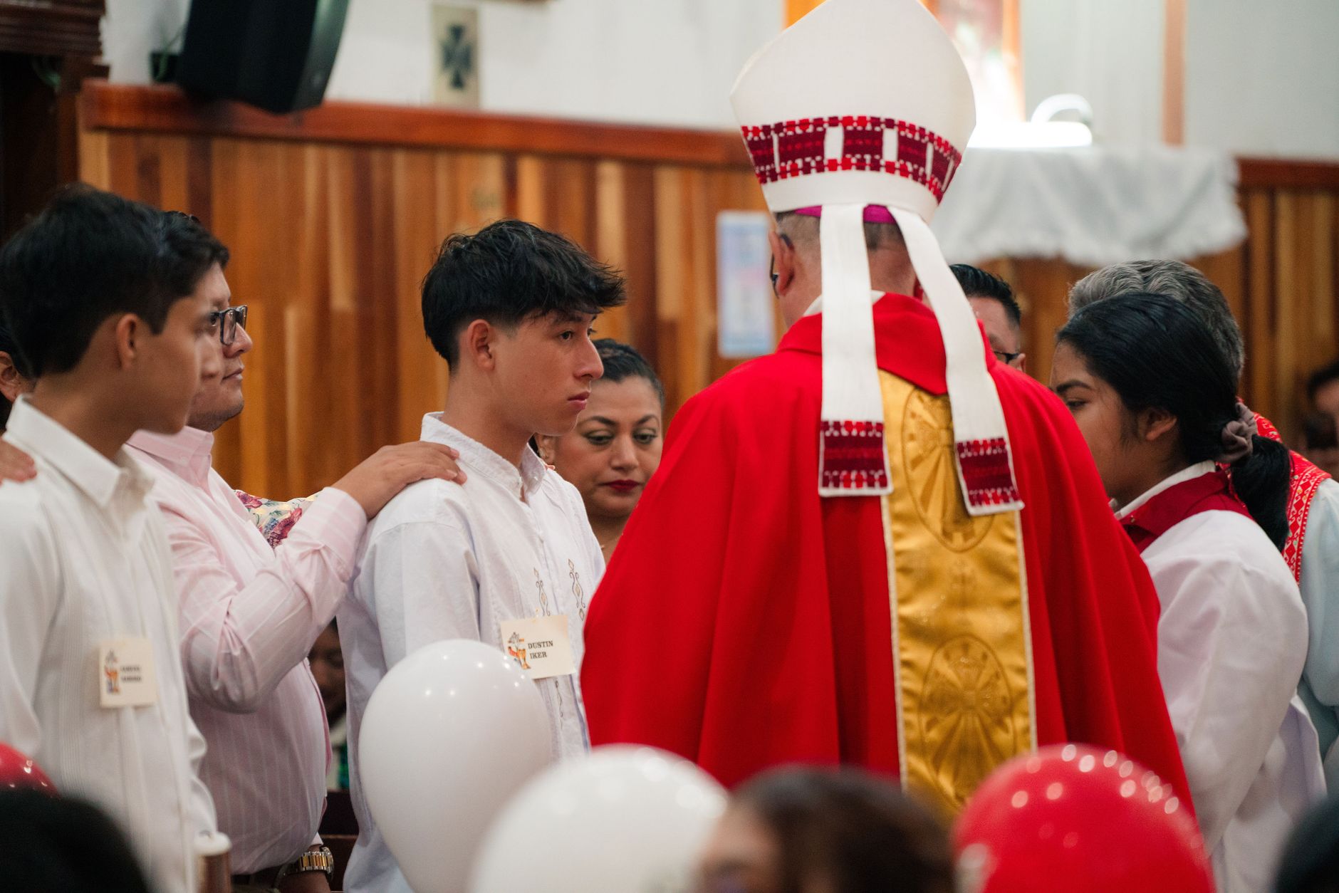 Catholic bishop leading a confirmation ceremony with participants in traditional attire.