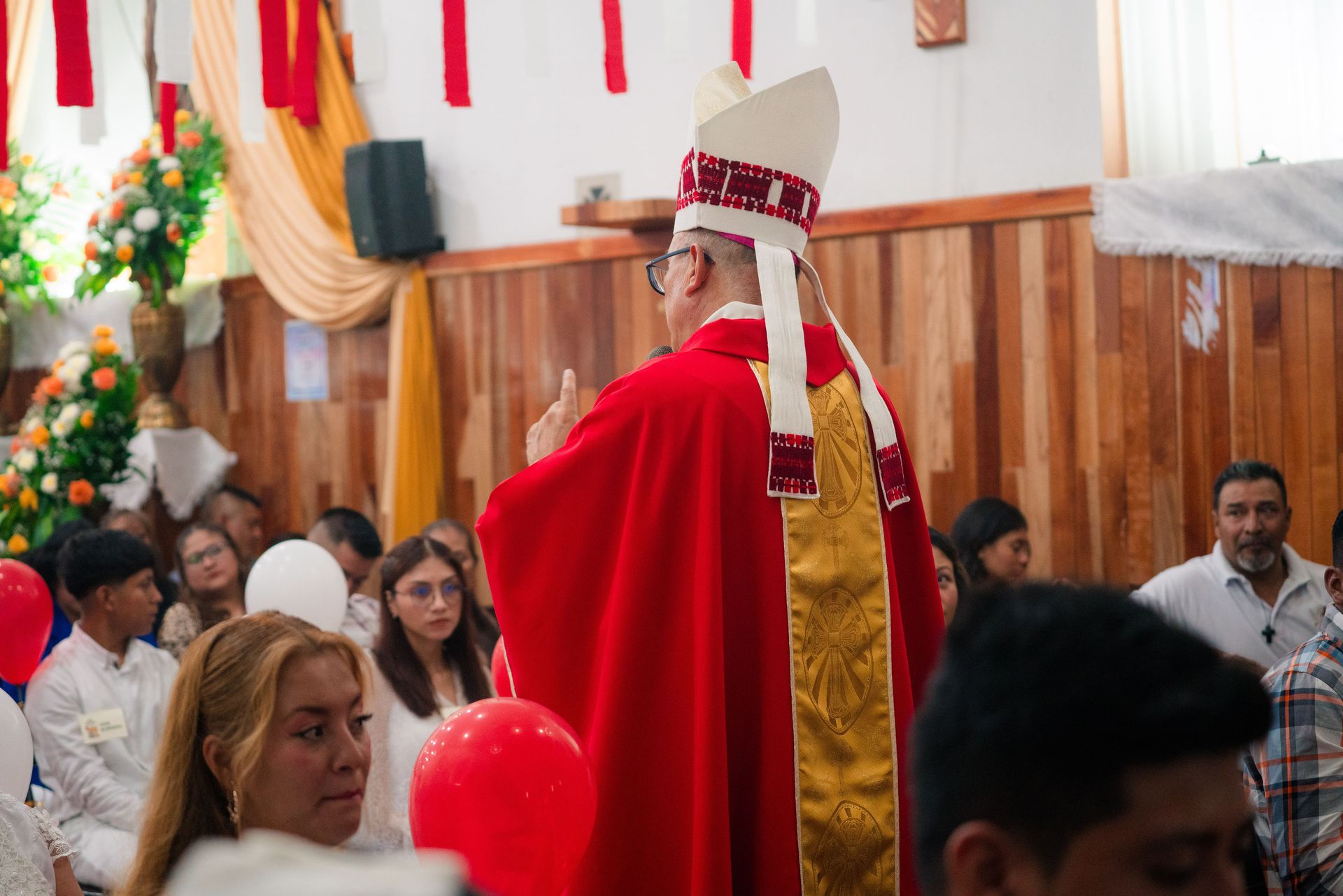 Bishop in red robe conducting a ceremony inside a church with attendees.