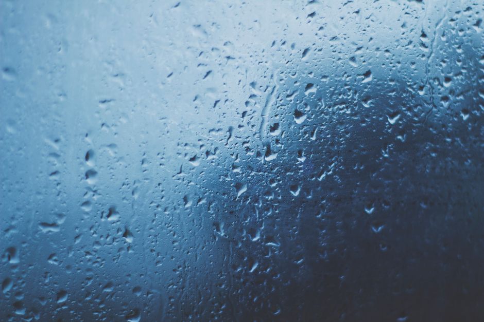 Detailed view of water droplets on a glass window with a blue background.