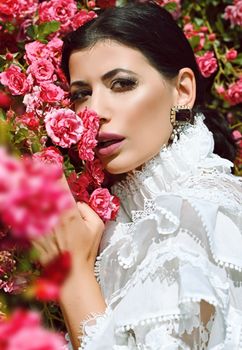 A stylish woman in a lace outfit poses elegantly among vibrant pink roses, showcasing beauty and nature.