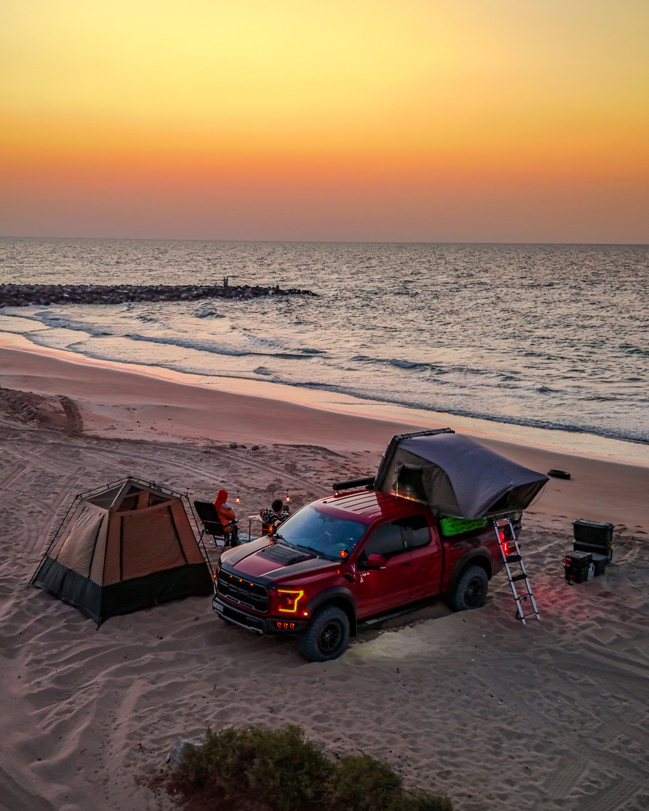 A vibrant red truck with rooftop tent on a serene beach at sunset, perfect for outdoor adventure.