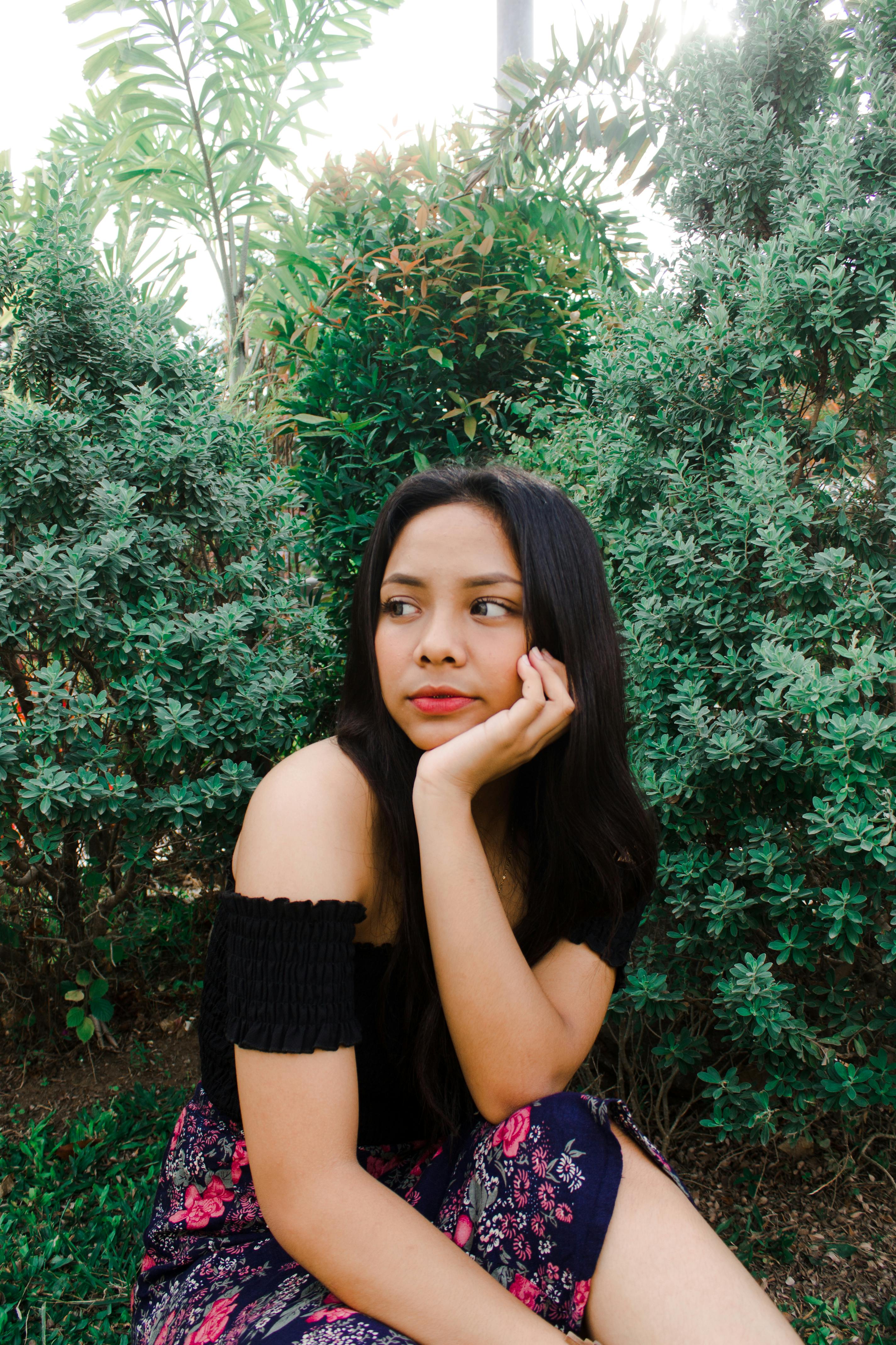 一位年轻女子穿着休闲装，在绿树成荫的公园里若有所思地放松身心