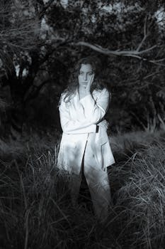 A woman in a white suit poses thoughtfully in a twilight forest setting.