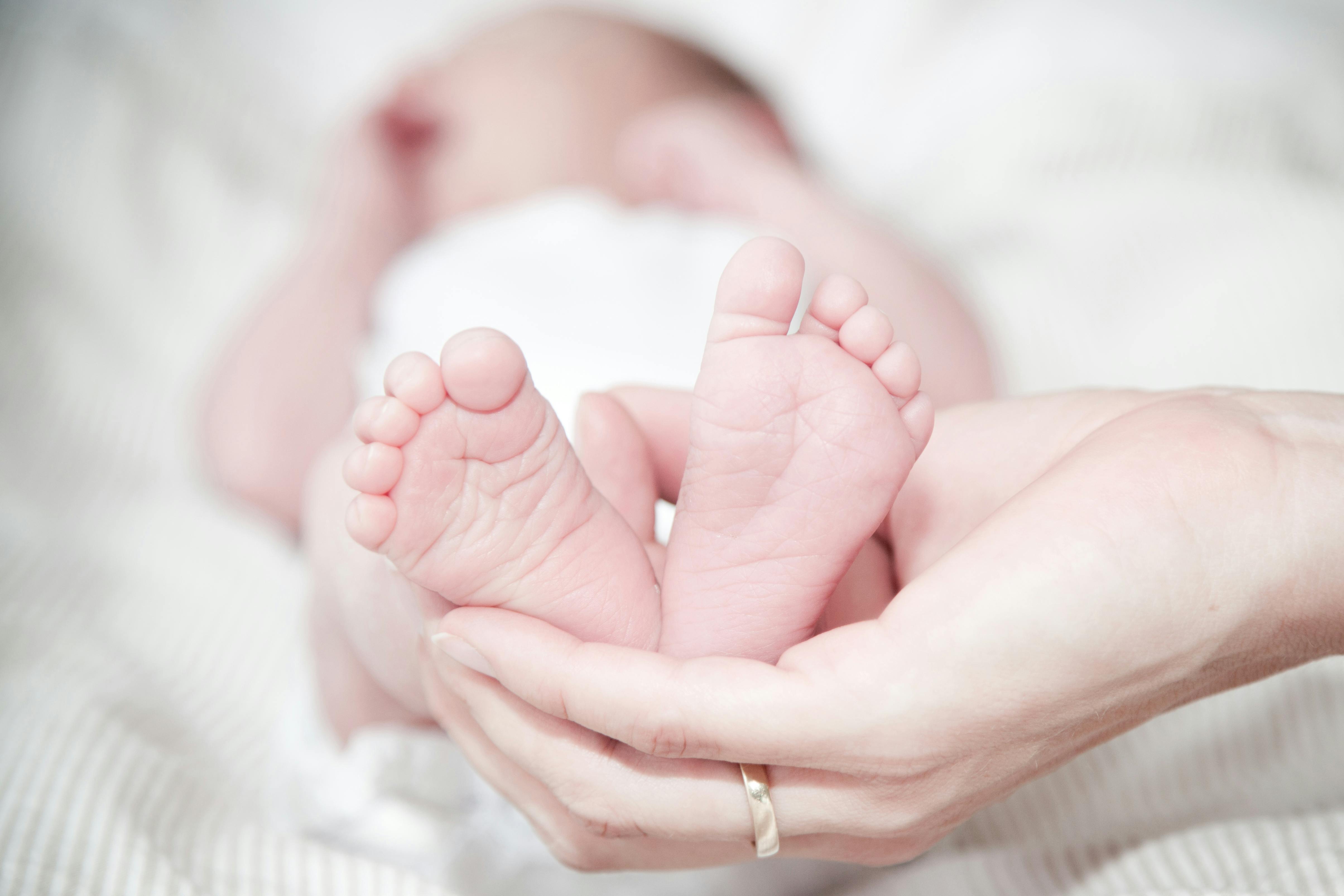 Closeup of mother hands holding cute tiny baby feet, showing baby foot.  Pink Background. Horizontal. Stock Photo