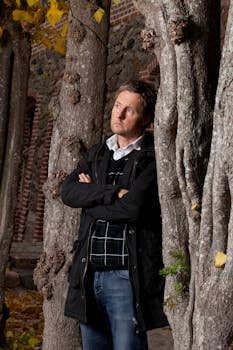 一个深思熟虑的人站在树林中，背景是砖房