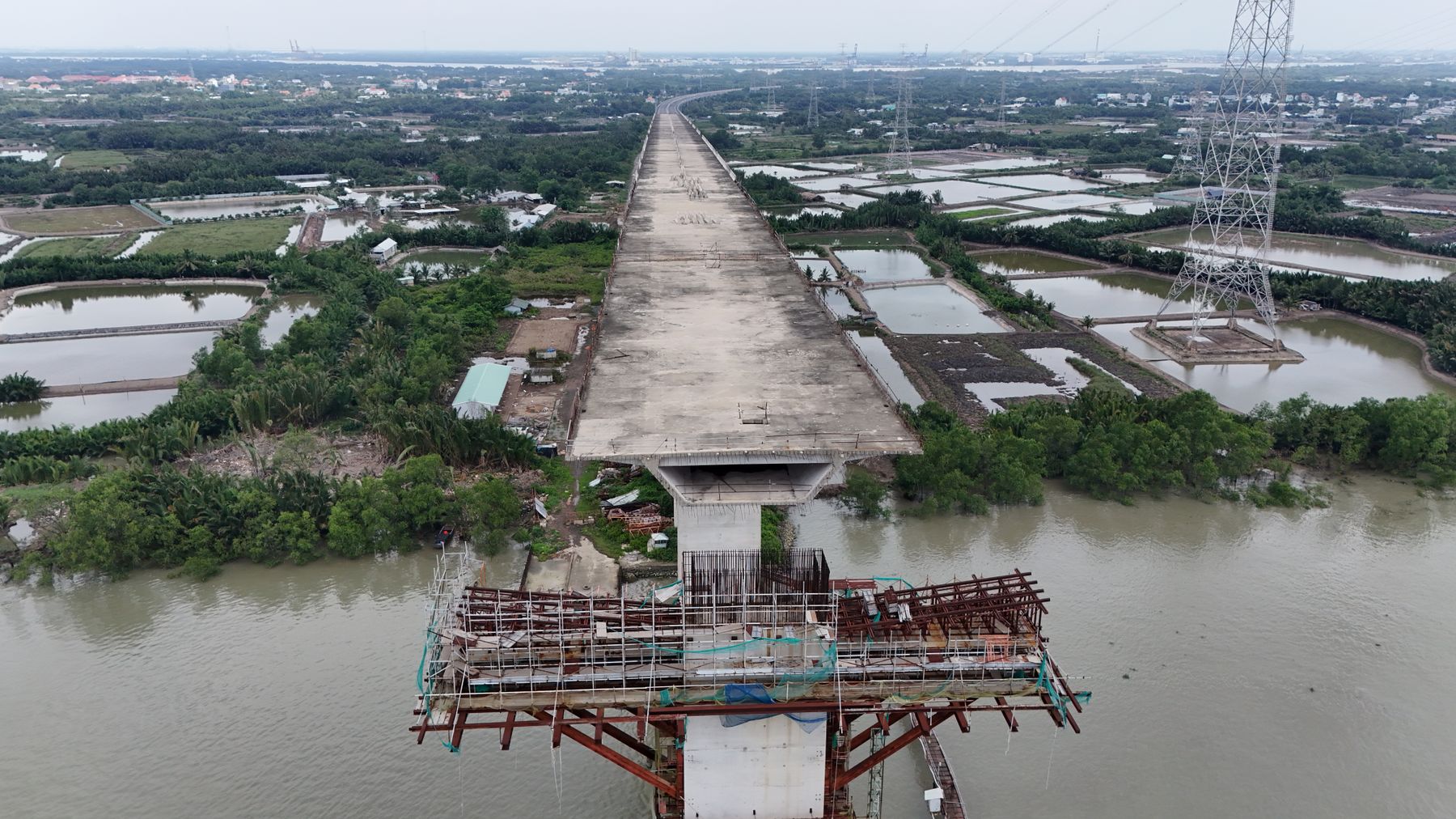An aerial shot of an unfinished bridge spanning a river with wetlands and rural landscape in Vietnam.