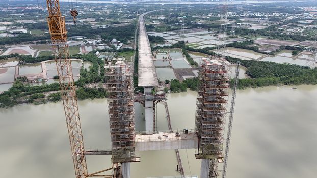 Aerial shot of bridge construction in Ho Chi Minh City, featuring cranes and scaffolding over a wide river.
