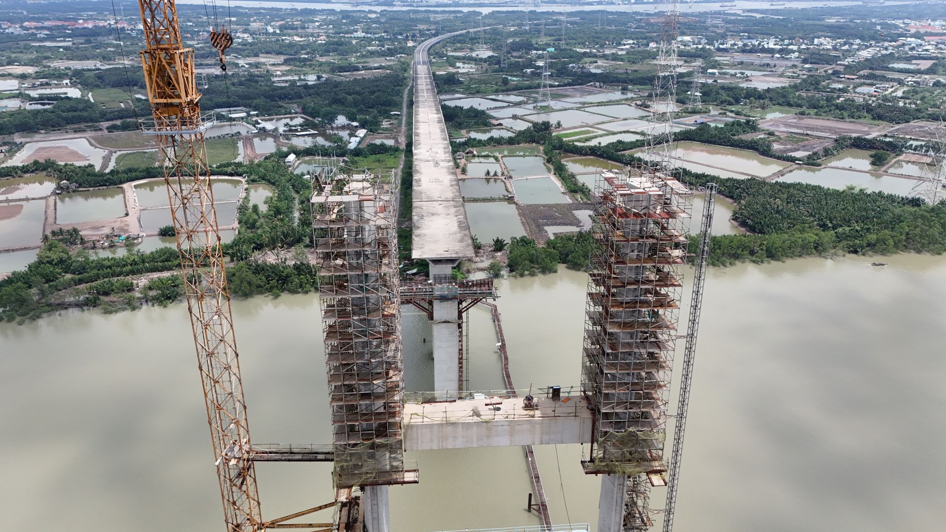 Aerial shot of bridge construction in Ho Chi Minh City, featuring cranes and scaffolding over a wide river.