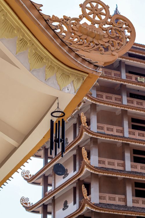 Free Close-up view of ornate temple roof with wind chimes against a multi-tiered building backdrop. Stock Photo